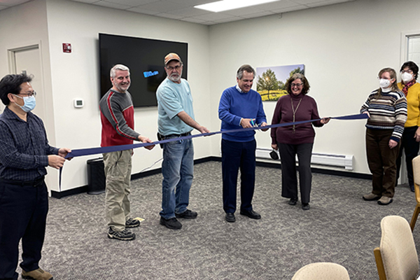 Members of the AMBS campus community hold a ribbon during a ribbon cutting ceremony for the updated Room 116 in Waltner Hall.