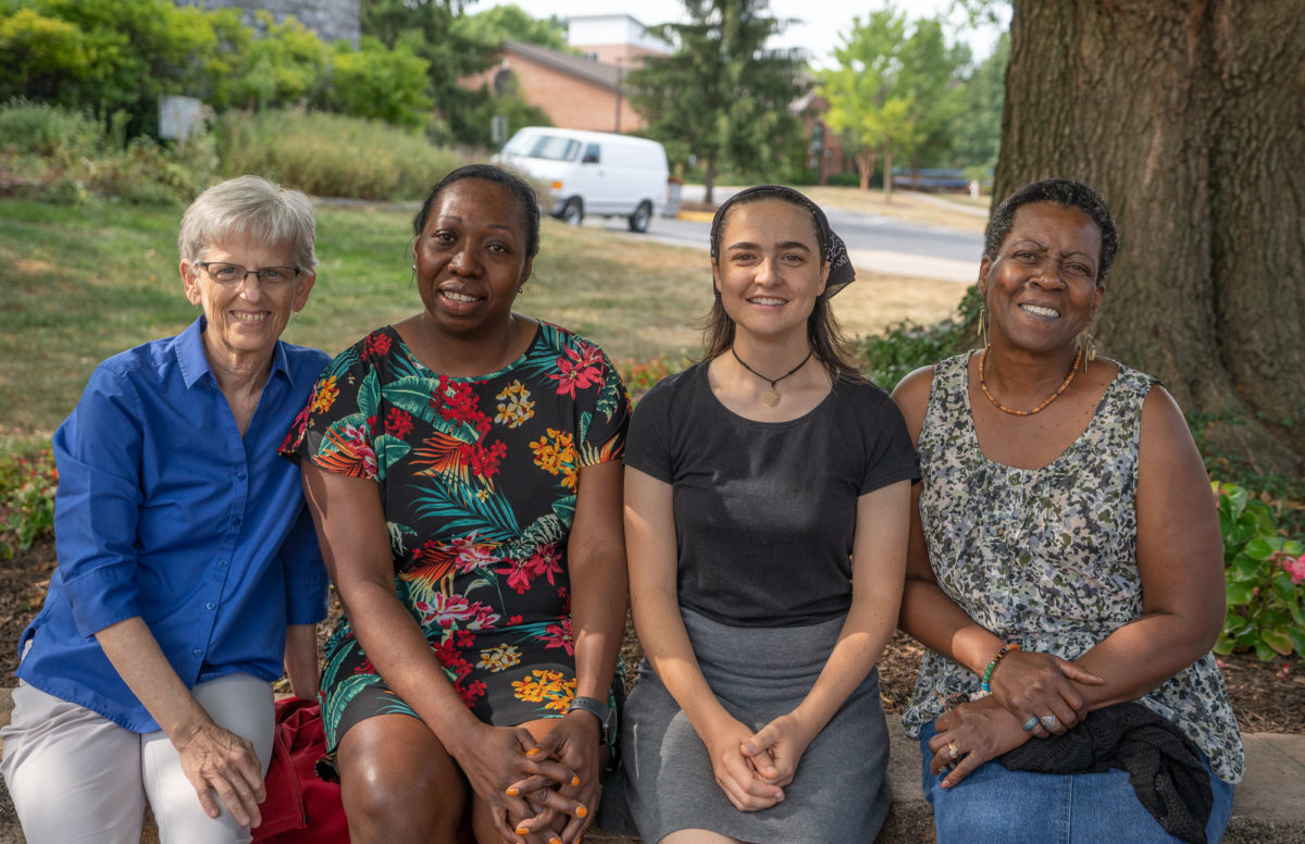 Four women sit in a row in front of a tree