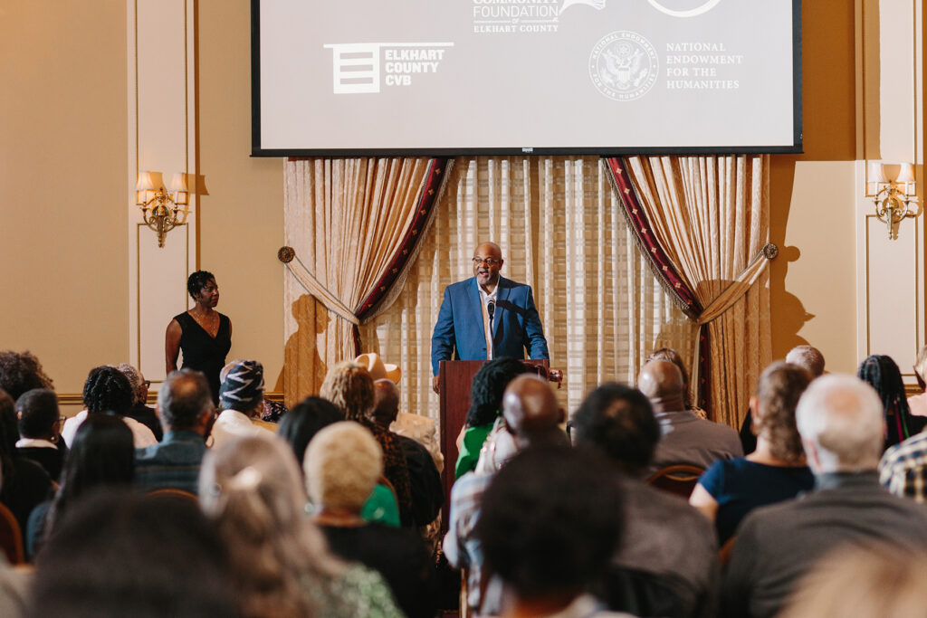Elkhart Mayor Rod Roberson addresses around 250 attendees at the documentary premiere of What Happened at Benham West: African American Stories of Community, Displacement and Hope on May 19, 2023, at the Crystal Ballroom at the Lerner Theatre in Elkhart, Indiana. Also standing are Nekeisha Alayna Alexis (at left), one of the project coordinators, and Oliver Pettis (at right), filmmaker. (Credit: Brittany Purlee)