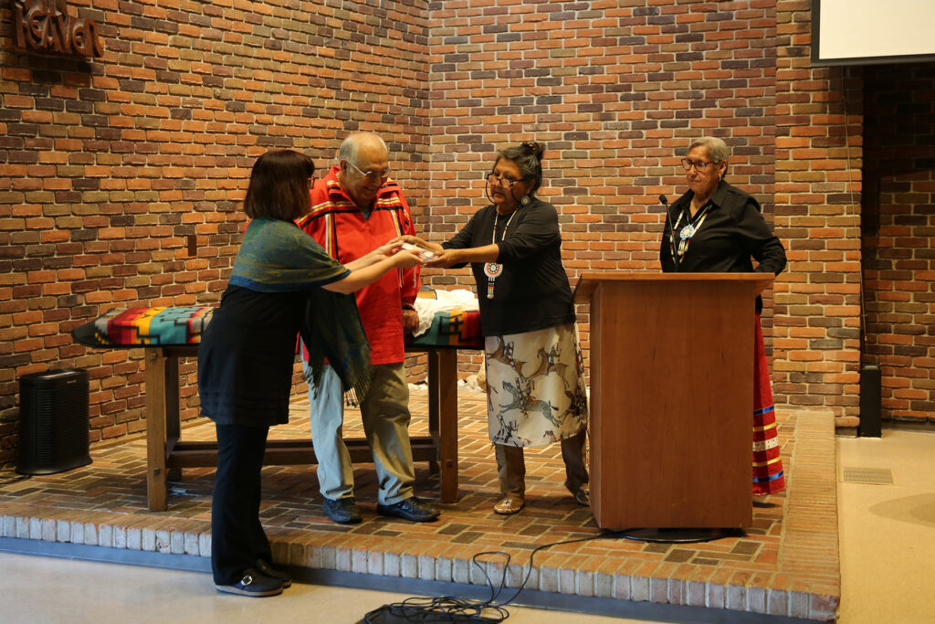 Rev. Susan Hart presents a gift of a hand-beaded cross to Beverly Lapp, AMBS Vice President and Academic Dean, during the Oct. 3 ceremony at Anabaptist Mennonite Biblical Seminary in Elkhart, Indiana. (l. to r.): Lapp, Dr. Richard Littlebear, Hart and Elder Wilma Redbird. (Credit: Abenezer Dejene)