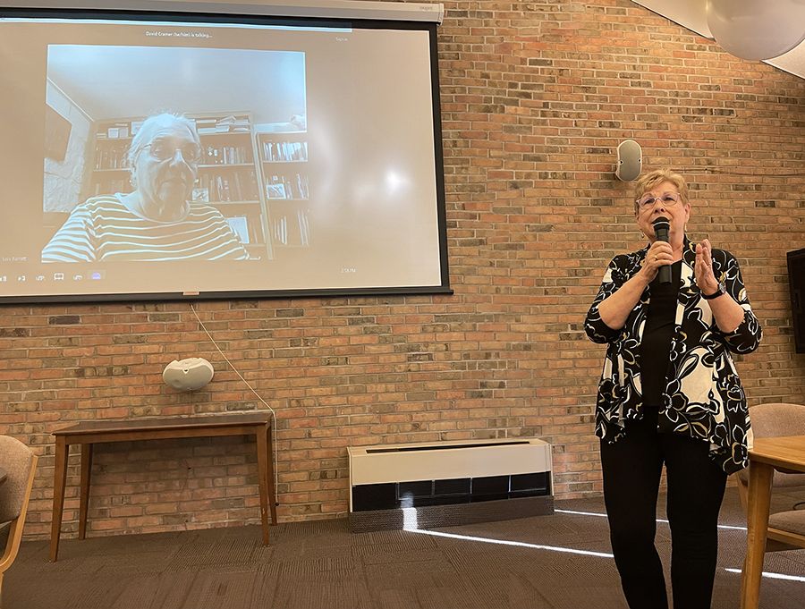 At a celebration of the release of Proclaiming the Good News: Mennonite Women’s Voices, 1972–2006 (Institute of Mennonite Studies, 2023) on Nov. 9 at Anabaptist Mennonite Biblical Seminary, editor Lois Barrett (on screen) and Dorothy Nickel Friesen (standing) shared about their process of creating the book. (Credit: Rachel A. Fonseca)